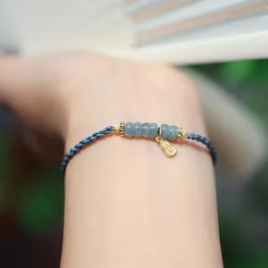 Makro-Detail eines handgewebten blauen Kordelarmbands mit grünen Jadeperlen und Goldanhänger