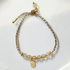 Detail von eisblauen Jadeit-Perlen und goldenem Fu-Anhänger am geflochtenen Armband