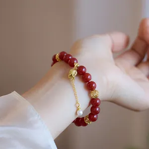 Gros plan d'un bracelet en agate rouge avec pendentif tulipe doré et perle au poignet