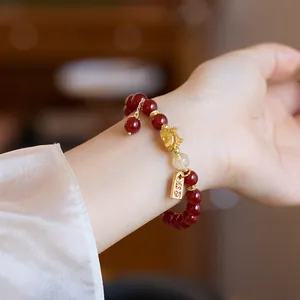 Détail du bracelet en agate rouge avec breloque tête de lion dorée et pendentif chance