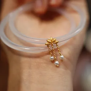 Detail eines Chalcedon-Armreifs mit goldenem Lotus-Anhänger und Perlenquasten