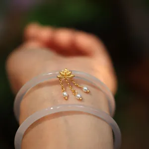 Detail von weißen Chalcedon-Armreifen mit goldenem Lotus-Anhänger und Perlen in der Natur