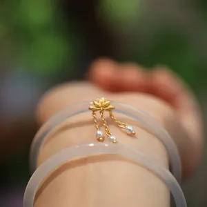 Detailaufnahme von Chalcedon-Armreifen mit goldenem Lotus-Anhänger und Perlenfransen