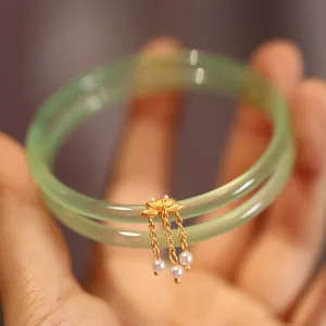 Detail von hellgrünen Chalcedon-Armreifen mit goldenem Lotusblüten- und Perlenquastenanhänger