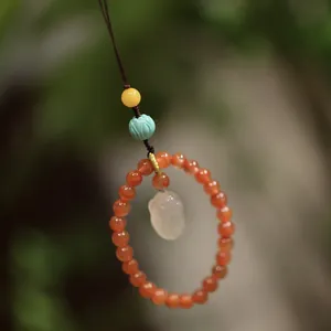 Close-up of natural red agate beads with a hand-carved jade pendant on brown cord