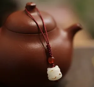 Macro detail of white chalcedony lucky cat charm and red bead hanging on a teapot