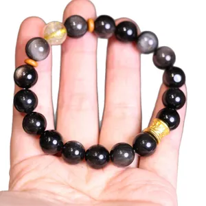 Pulsera de obsidiana natural con cuarzo rutilado dorado en mano, joyería elegante
