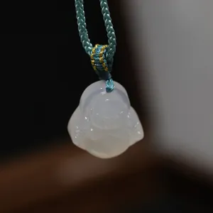 Macro view of white agate Maitreya Buddha pendant with blue woven silk cord