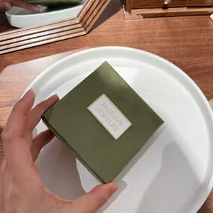 Top view of a square matcha green velvet jewelry box with gold label held by a person