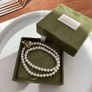 Detail of white pearl necklace with green velvet jewelry box on white ceramic tray