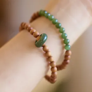 Detail of sandalwood and jade bead bracelets set featuring a green jade donut charm