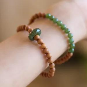 Close-up of sandalwood beads and green jade ring bracelet on wrist with warm lighting