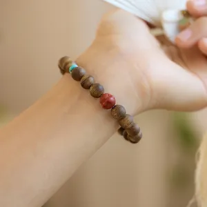 Dettaglio del bracciale in legno di agar naturale con perla rossa su ventaglio bianco