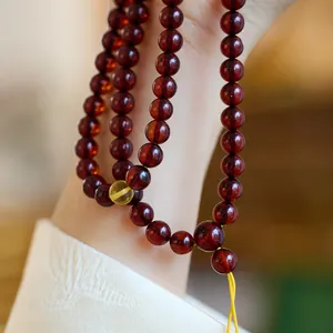 Bracelet ambre à trois tours en brun rouge foncé avec perle jaune porté au poignet