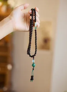 Macro detail of sandalwood prayer beads with jade accents and enameled cloud charm