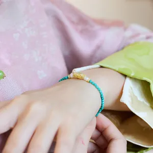 Detailopname van turquoise parelarmband met zilveren ruyi-bedeltje om de pols