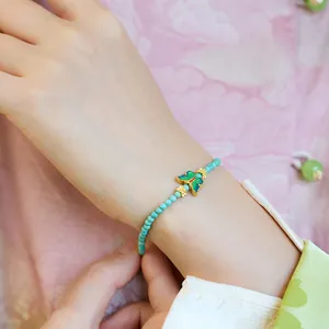 Detail van kralenarmband met turkoois en kleurrijke emaille vlinder aan de pols hangend