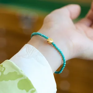 Detailopname van turquoise armband met gegraveerde gouden kraal op zijden stof achtergrond