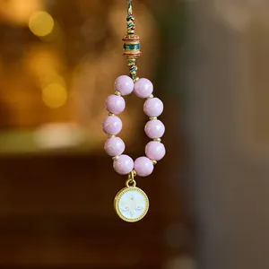 Close-up of a spiritual phone charm with pink beads, gold accents and Buddha eye pendant