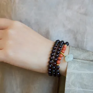 Detail of multi-layer sandalwood bead bracelet with green jade flower pendant on wrist