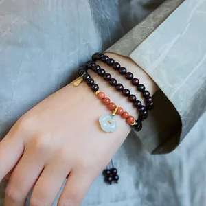 Detail of multi-layer wood bead bracelet with green jade Ruyi pendant on wrist