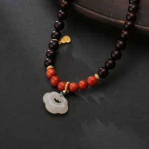 Detail of sandalwood necklace with white jade pendant and gold lucky charm on dark wood