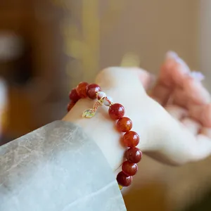 Gros plan d'un bracelet en agate veine de dragon avec pendentif poisson doré au poignet