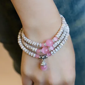 Macro detail of multi-layer natural seed bracelet with pink cat eye stone and silver charms