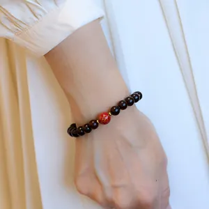Detail view of sandalwood beaded bracelet with red lacquer bead on female wrist