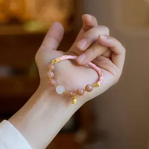 Natural sunstone bracelet with lily of the valley charm and pink enamel on a woman's wrist