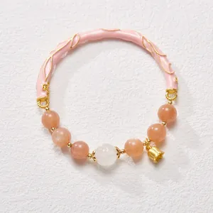 Detail of sunstone bead bracelet featuring pink enamel cuff and golden bell charm