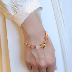Detail of sunstone bead bracelet with a golden lily of the valley charm on wrist