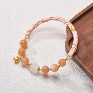 Detail of sunstone bead bracelet with pink enamel bangle and gold lily charm