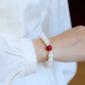 Close-up of white bodhi seed bracelet with a red cinnabar bead on a silk sleeve