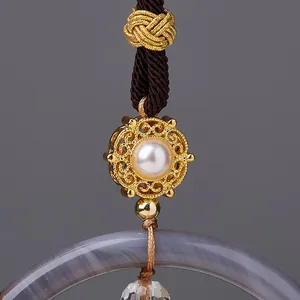 Macro shot of sandalwood car pendant with gold filigree, pearl, and grey agate ring