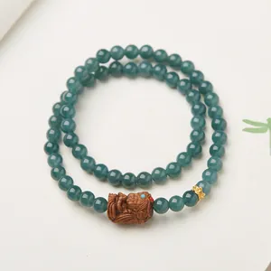 Détail du bracelet double en jade bleu avec bête en bois sculpté et breloque lotus dorée