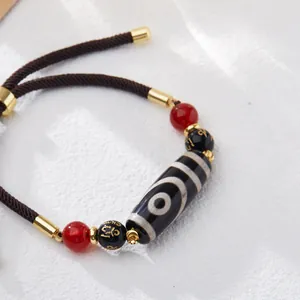 Macro shot of Tibetan nine-eyed agate Dzi bead on woven rope bracelet with gold accents
