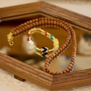Détail macro du collier en bois de santal et bracelet perle Dzi sur miroir
