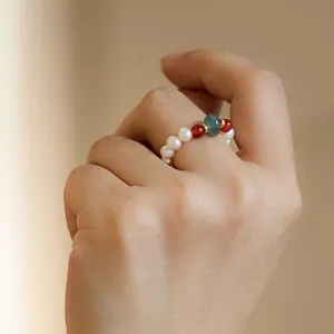Handmade freshwater pearl ring with green emerald stone and red accents on finger