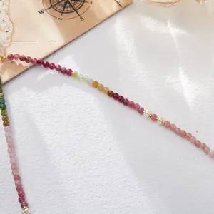 Detalle de collar de turmalina de colores con perlas y toques dorados sobre fondo blanco