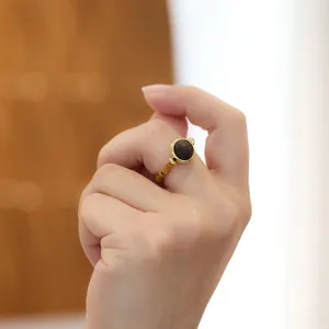 Bague dorée style bambou avec perle foncée portée à l'index sous lumière naturelle