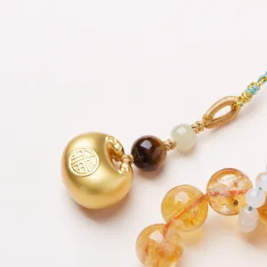 Macro detail of yellow citrine beads and golden Fu lock pendant on braided cord