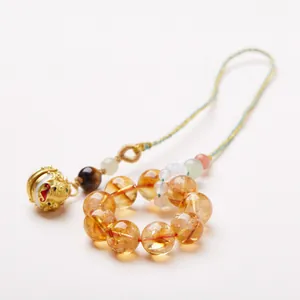 Natural yellow crystal bead charm with gold tiger bell on a white minimalist background