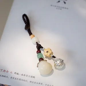 Macro detail of hand-woven keychain with white Bodhi gourd pendant and small silver bell