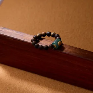 Agarwood beaded ring with green jadeite cylinder and gold pattern on wooden base