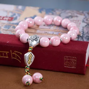 Rosa glasiertes Keramikperlenarmband mit Blumenanhänger auf Vintage-Büchern