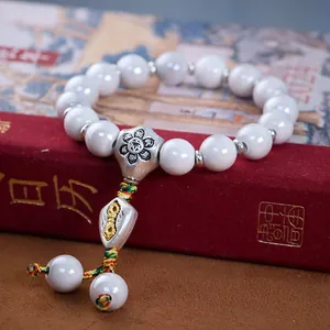 Detail eines Perlenarmbands mit weißen Porzellanperlen und silbernem Dorje-Vajra-Anhänger