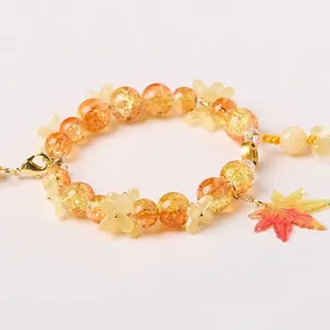 Macro detail of beaded bracelet with orange crackle beads and a maple leaf pendant