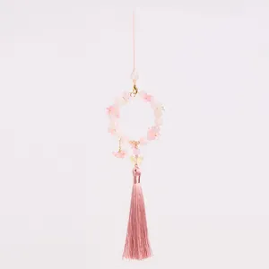 Detailed view of pink beaded charm with glass flower, butterfly, and long silk tassel