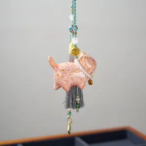 Macro detail of a pink ceramic cat charm with gold speckles and a gray silk tassel